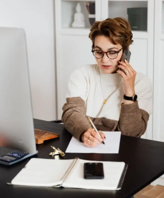 Admin VA A woman writing on a notebook while talking on the phone.