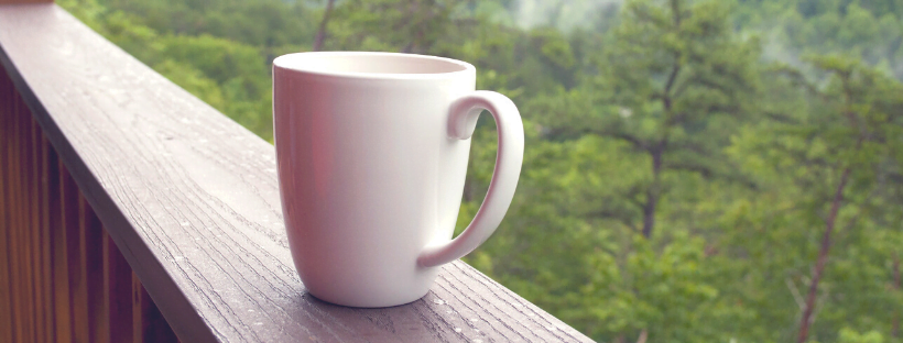 A mug kept on a railing with trees in the background.