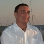A photo of Steven Zoernack smiling, wearing a white tee-shirt.He looks away from the camera.