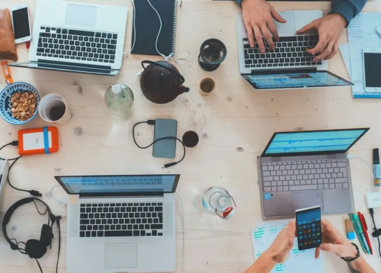 Top-down view of four people sitting at a breakfast table and working on their phones and laptops.