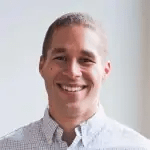 A photo of Isaac Odim smiling. Wearing an off-white shirt, with the neck button open.