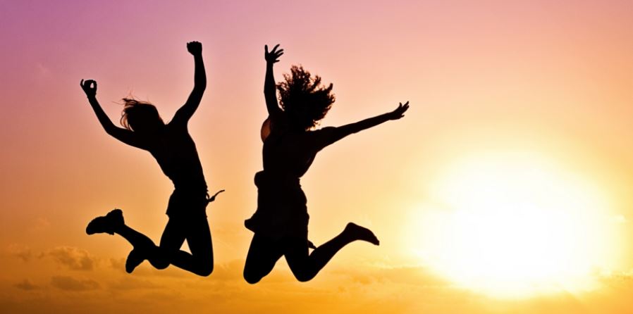 A silhouette of two people caught midair after having jumped, against a setting sun in the background.