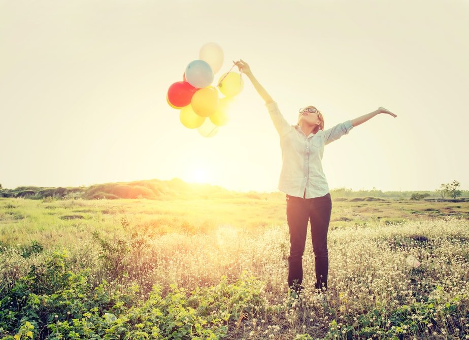 A decorative image of a woman holding a bunch of balloons and stretching her body out covered in sunlight.