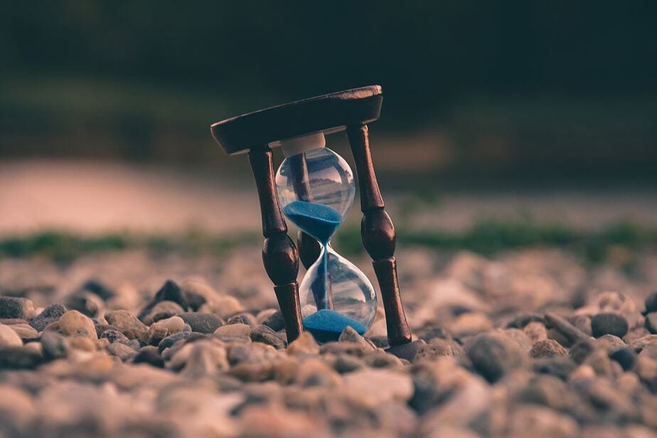 A partially sunk hourglass clock in sand.