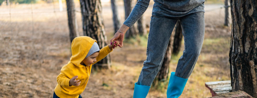 Mom helping her kid walk in a public park.