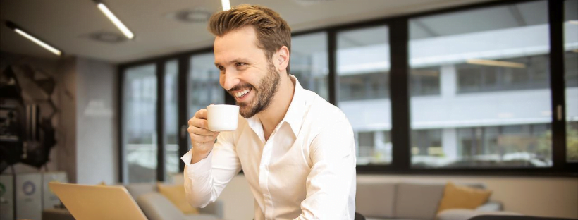 social A person sitting in a co-working-like space, drinking his coffee and smiling at someone or something.