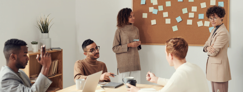 Brainstorm People in the office around a desk and in front of a board brainstorming and having discussions.