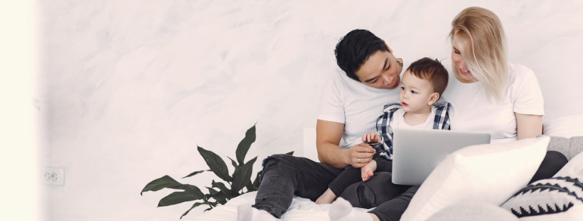 A couple playing with their child, while the mother works on her laptop.