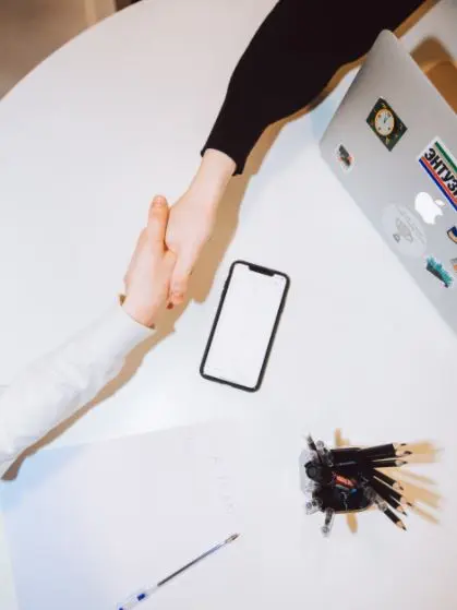 handshake Top-down view of a handshake. An iPhone and a bunch of keys rest in the center. An Apple laptop is also visible partially.