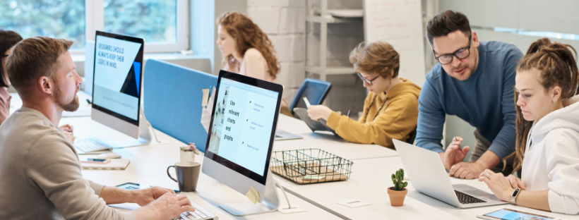 people working People, facing each other, working together at a desk on Apple iMac desktop computers.