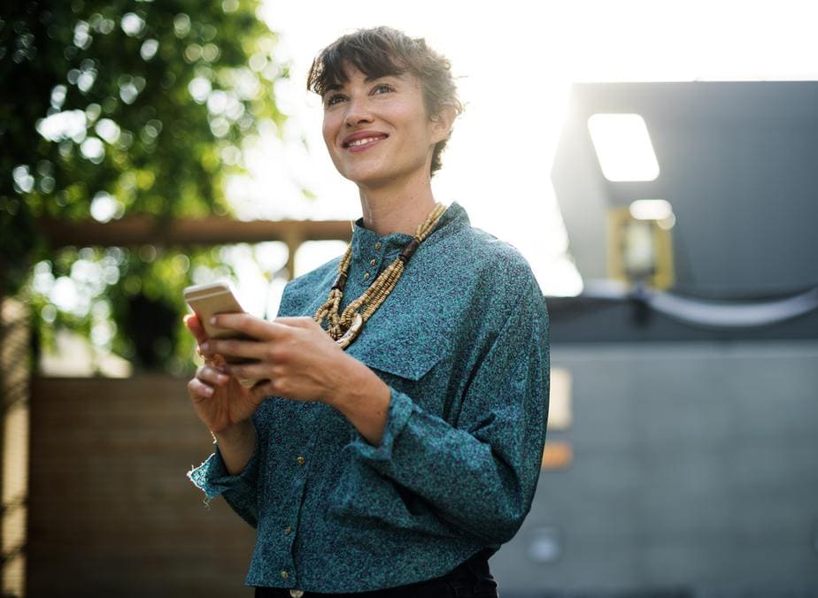 A woman wearing a dark ocean blue shirt looking up hopefully, while the sun beams from up behind.