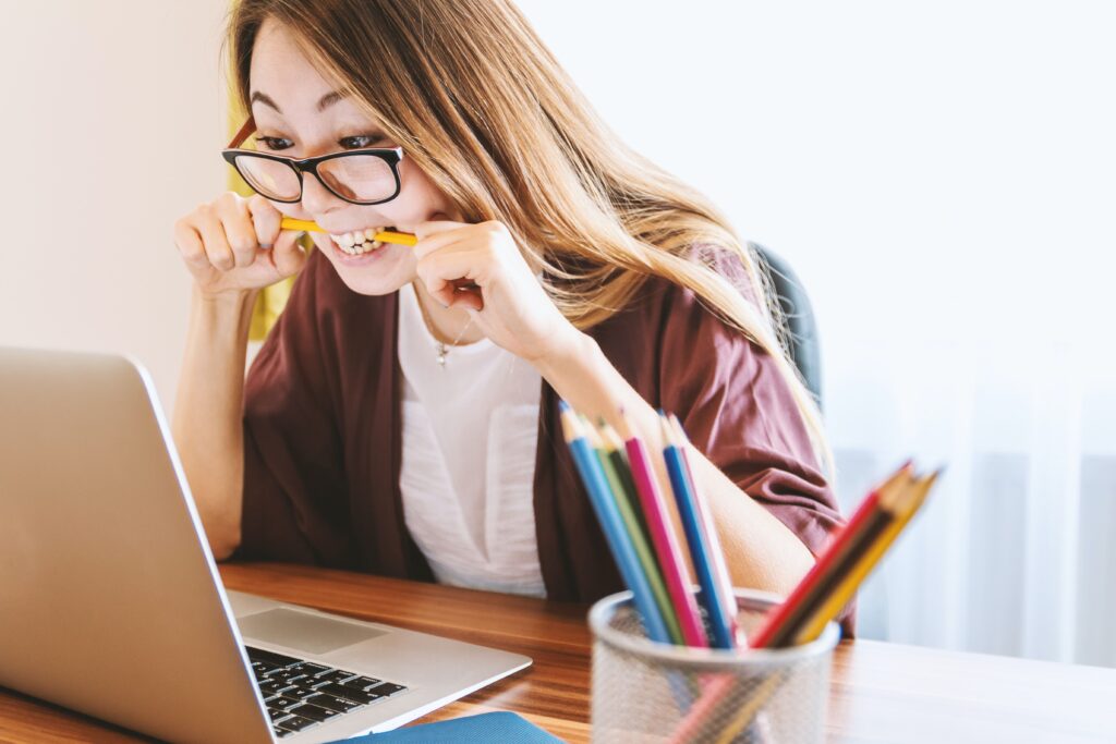 Creative VA Woman looking at a laptop while biting a pencil in frustration.