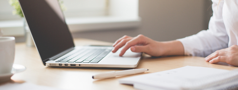 A virtual assistant working at her workplace with a laptop. A notebook and a pen are kept alongside.