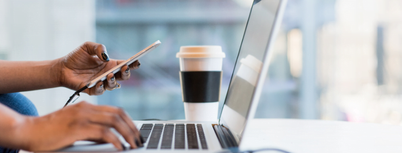 A virtual assistant working with her laptop and mobile phone. Coffee mug rests nearby.