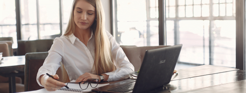 Woman going through some content on her physical notebook along with her laptop, in an empty office.