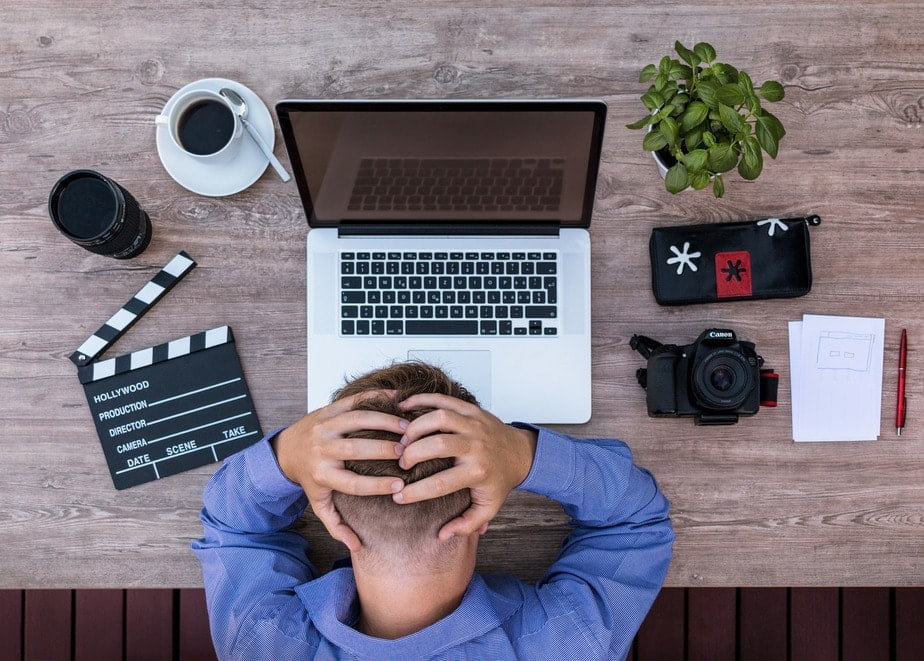 A man wearing a blue shirt holding his head in stress and anxiety.